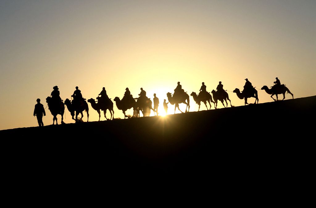 A photo taken on September 3, 2023, shows visitors riding camels through the desert in Dunhuang, Gansu Province. /CFP